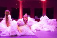 performers from La Ribalta Theater take part in a production. four girls are on stage, one looking forward, three looking backwards, all wearing white dresses