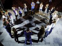 A group of young people stand in a cirle with their hands to their faces in an acting exercise.