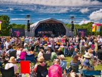 A large crowd in front of a stage at an outdoor summer music festival in England, UK.