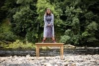 A woman in a dressing gown standing on a table by a river bed