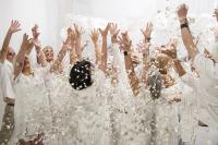 Image of people dressed in white, hands aloft, with white confetti/petals falling