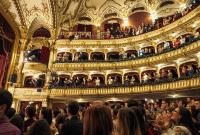 People giving a standing ovation to a performance in a theatre auditorium. Visible are the stalls, dress circle, upper circle and balcony.