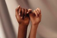 A close up two female hands, one black one white, locked in a "pinky promise" gesture