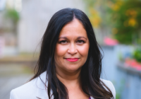 Mel Rodrigues, a woman with long dark hair wearing a light grey suit jacket