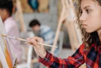 Young woman sits facing a canvas, creating a painting with oil colours