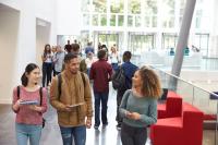 Students holding tablets and phone talk in university lobby