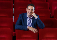 Lee Henderson sits on red seats in an auditorium