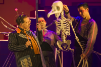 Performance of Welsh National Opera's The Magic Flute. three actors are on stage surrounding a skeleton