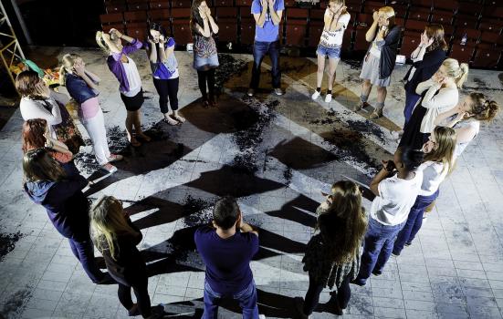 A group of young people stand in a cirle with their hands to their faces in an acting exercise.