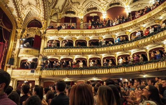 People giving a standing ovation to a performance in a theatre auditorium. Visible are the stalls, dress circle, upper circle and balcony.