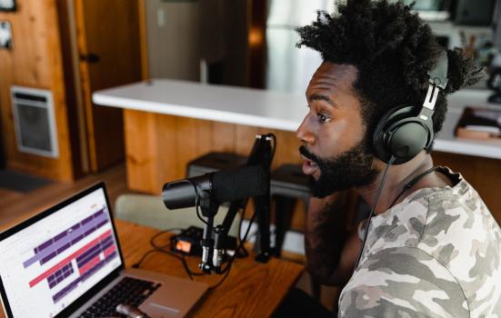 Man with headphones and microphone recording on a laptop