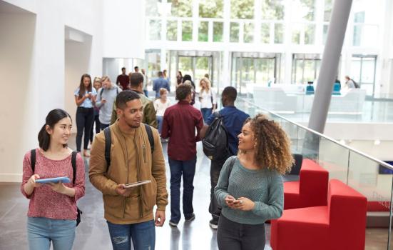 Students holding tablets and phone talk in university lobby