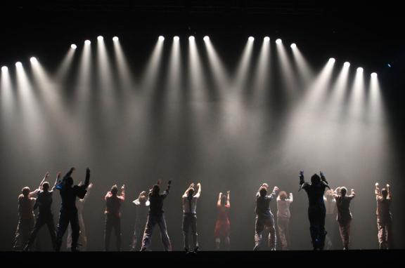 Performers on a stage looking up at multiple spotlights