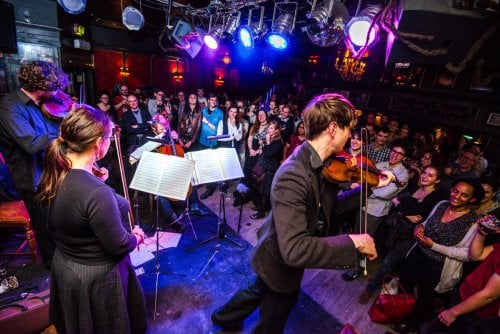 An orchestra performing in a small venue with a large crowd