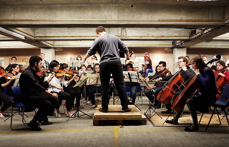 Photo of an orchestra playing in a car park