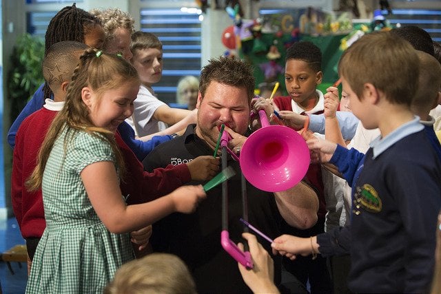 Photo of musician with pink trombone surrounded by school children