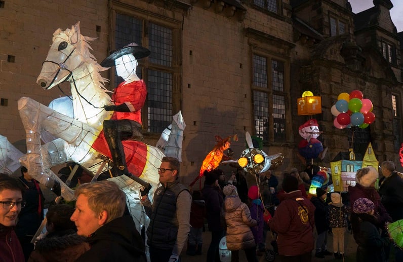 A crowd of people on a street holding illuminated paper sculptures