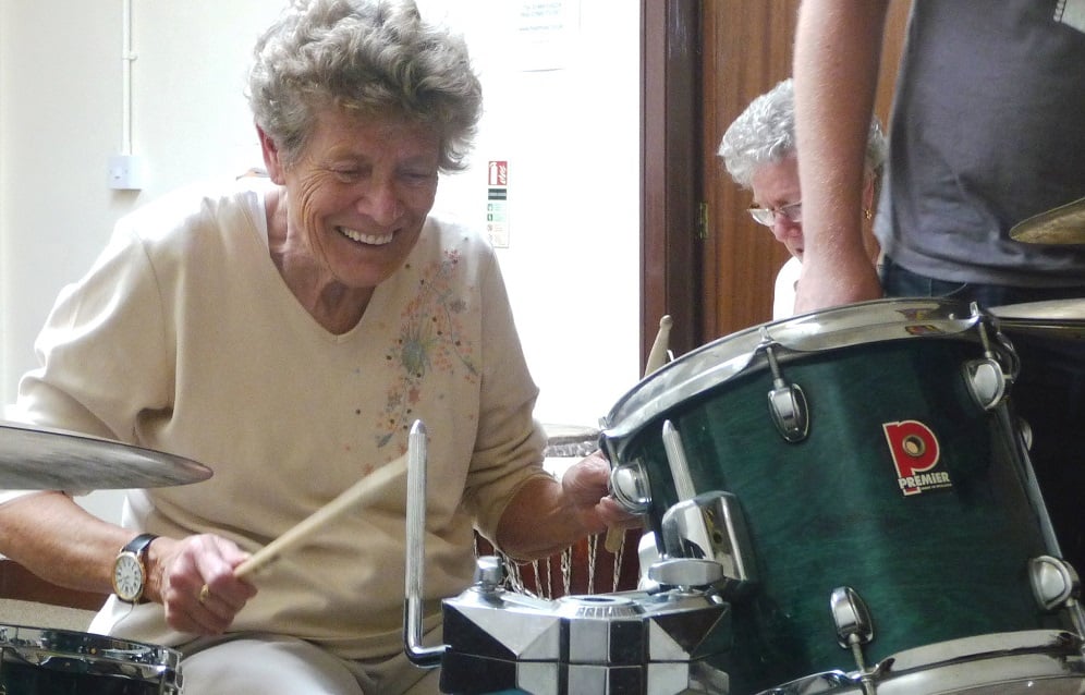 An older woman playing a drum kit