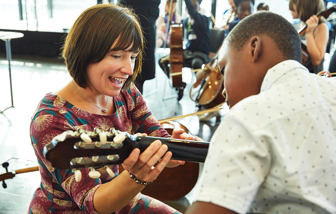 a young male learning acoustic guitar from a female