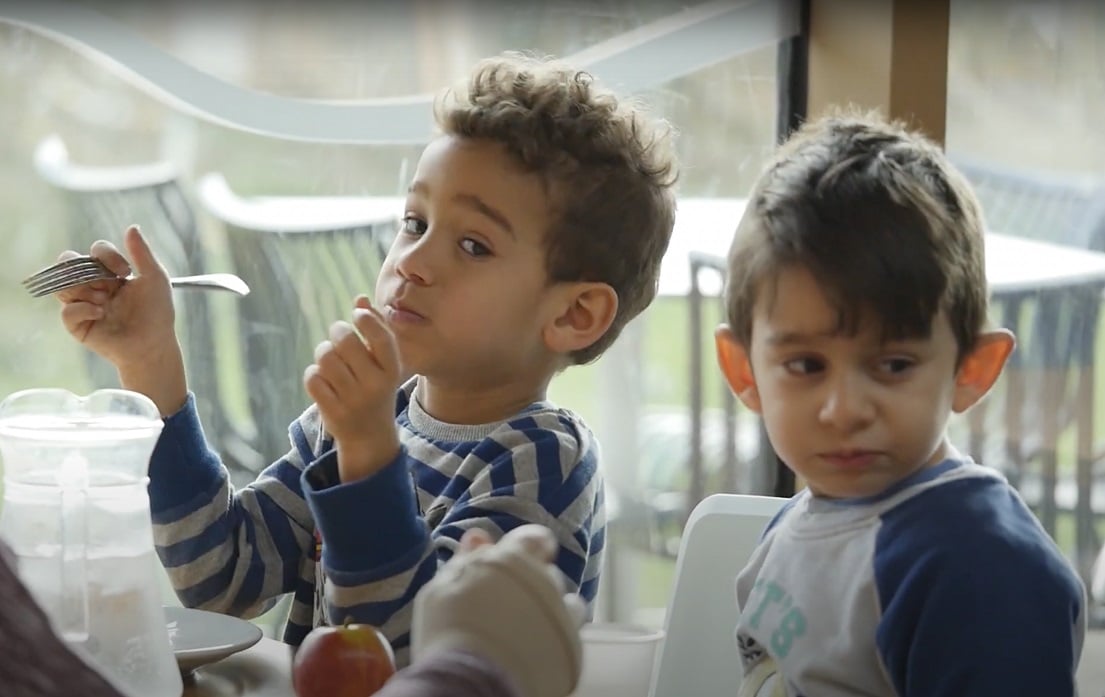 Two children eating at a canteen. One has spotted the camera and is giving the photographer side-eye