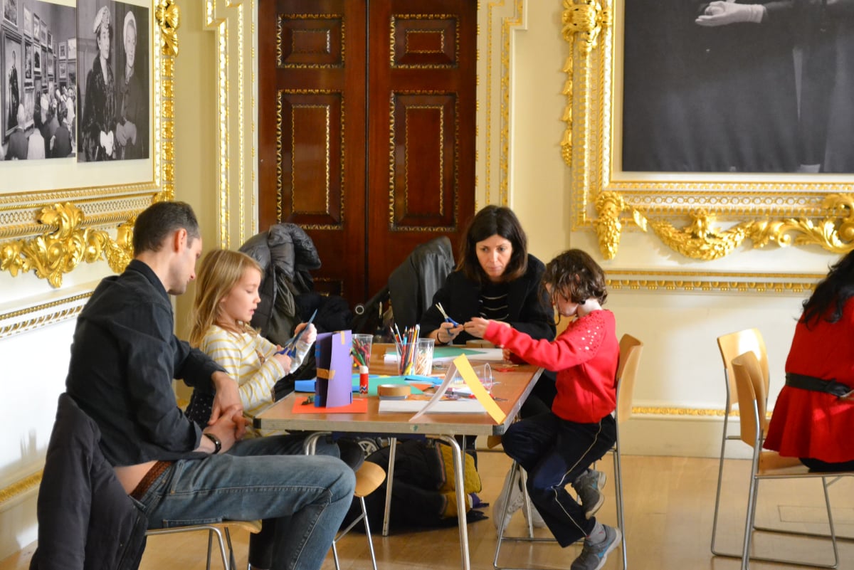 Two children at a desk working with two adults on crafts