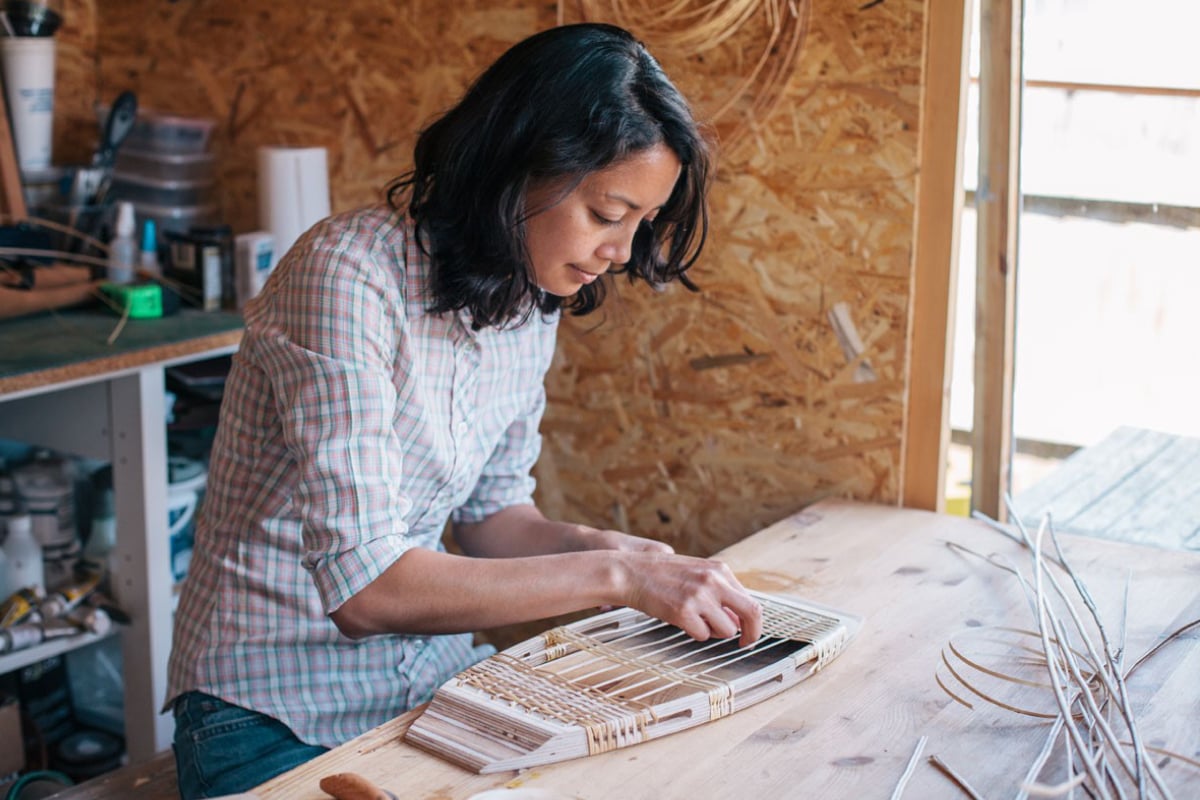 Woman weaving a chair seat inside workshop