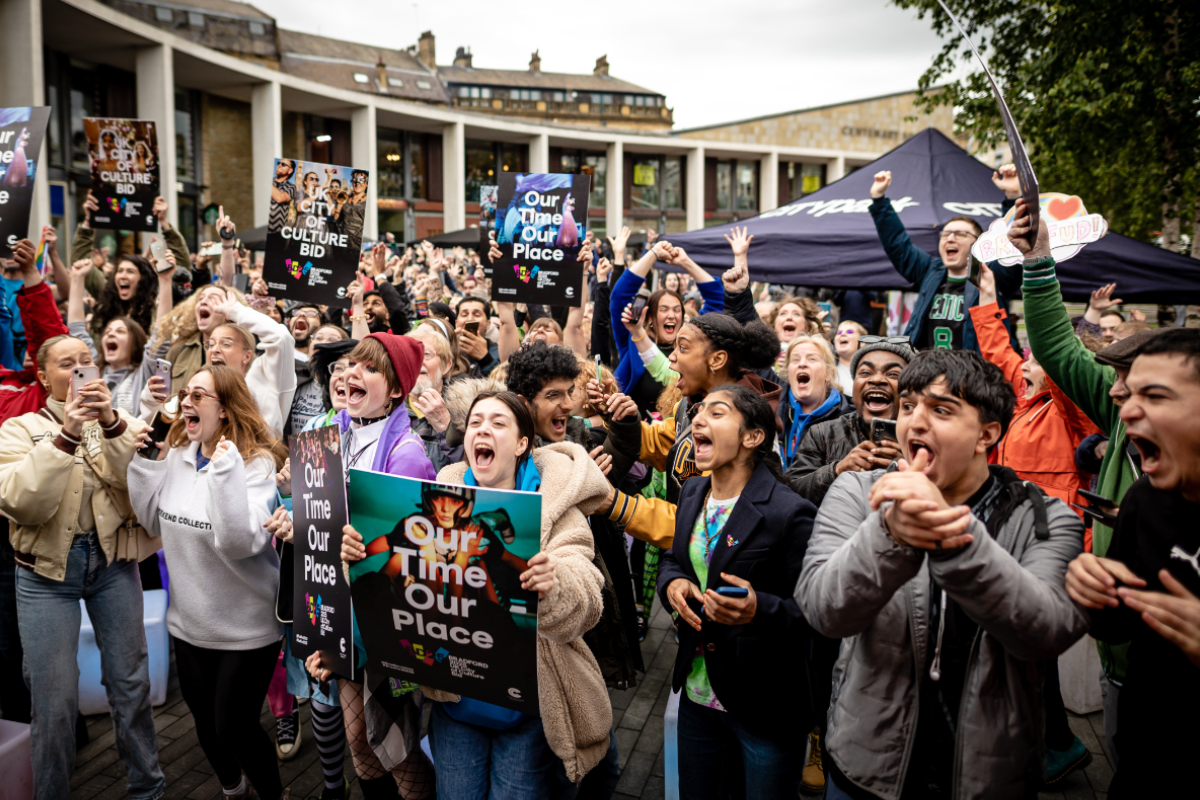 group of children celebrate Bradford winning UK City of Culture. they are jumping up and down, shouting, and holding banners saying 'our time, our place'