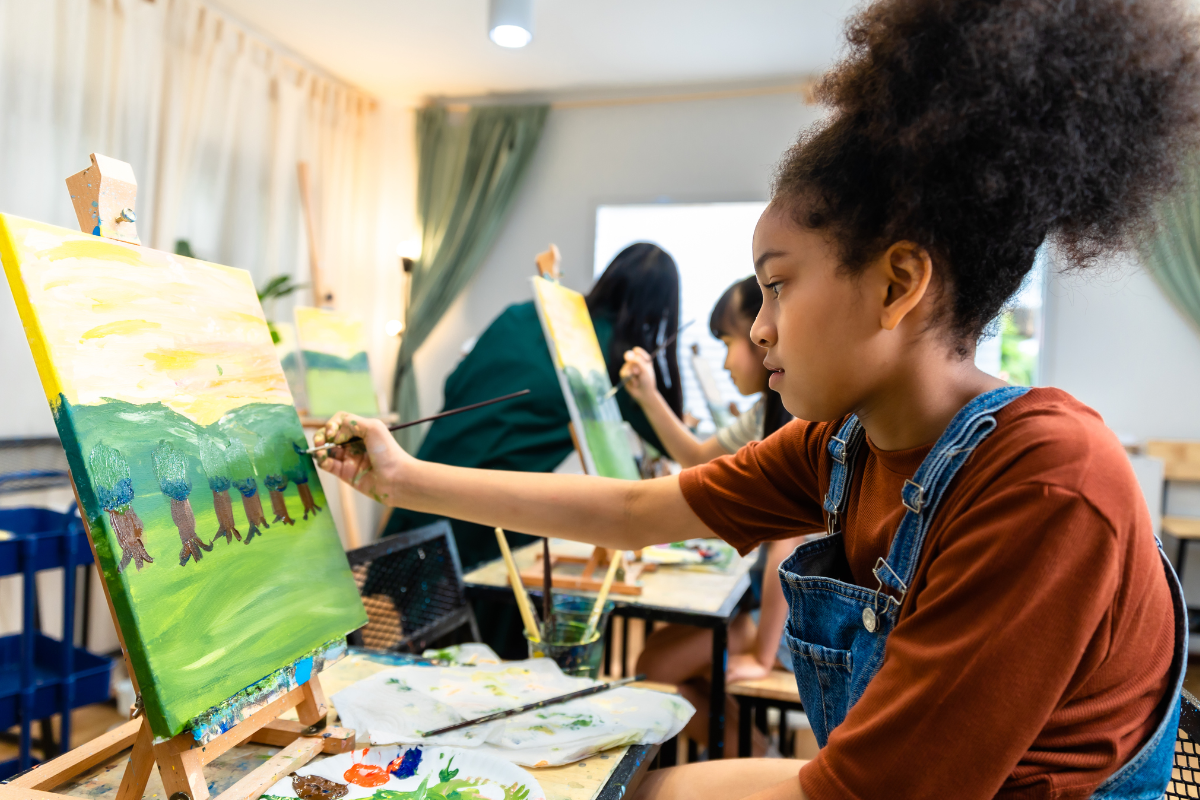 A school pupil takes part in an art class. she is painting a landscape with trees on a canvas