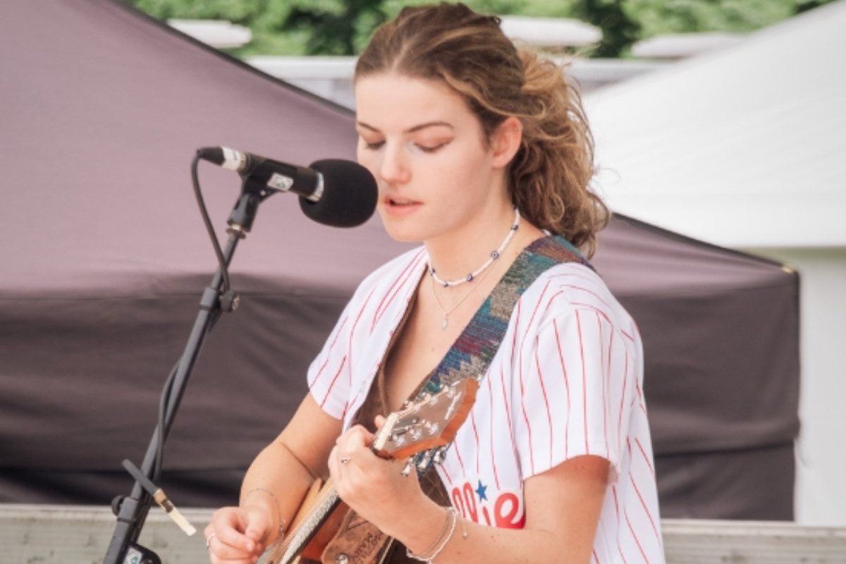 A young woman playing guitar and singing into a microphone