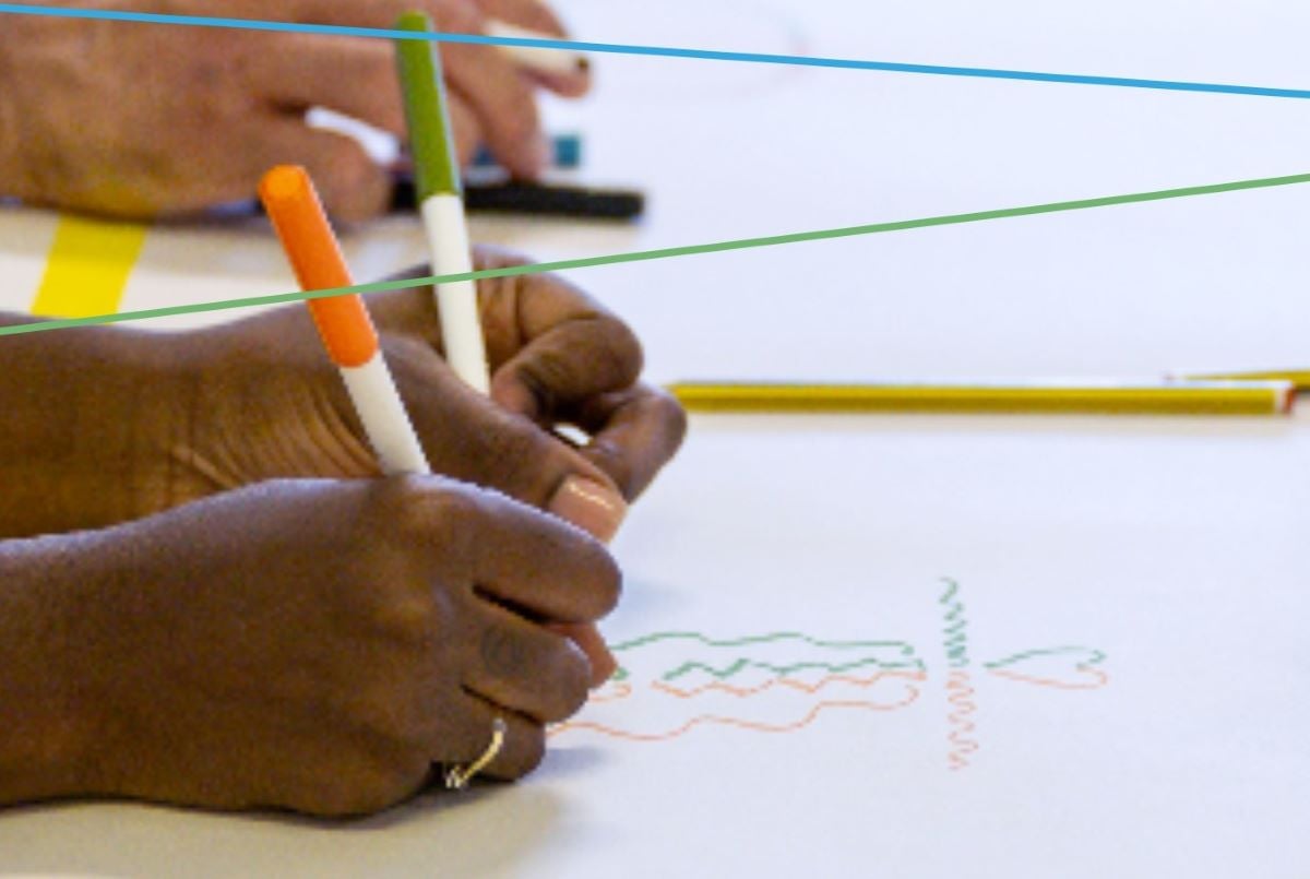 a photo close up of hands drawing with coloured markers on a blank piece of paper