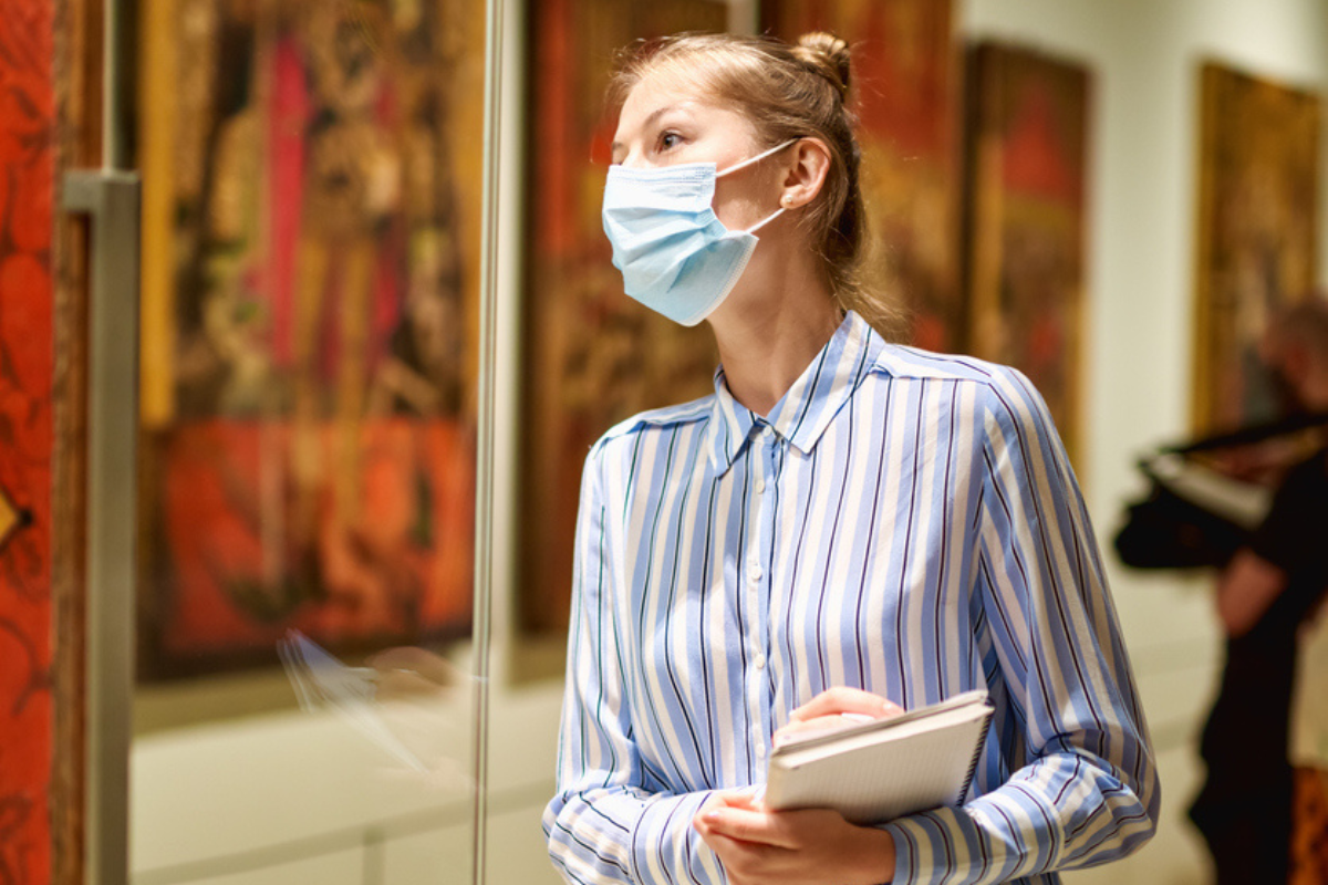 Woman visitor wearing an antivirus mask in the historical museum looking at pictures