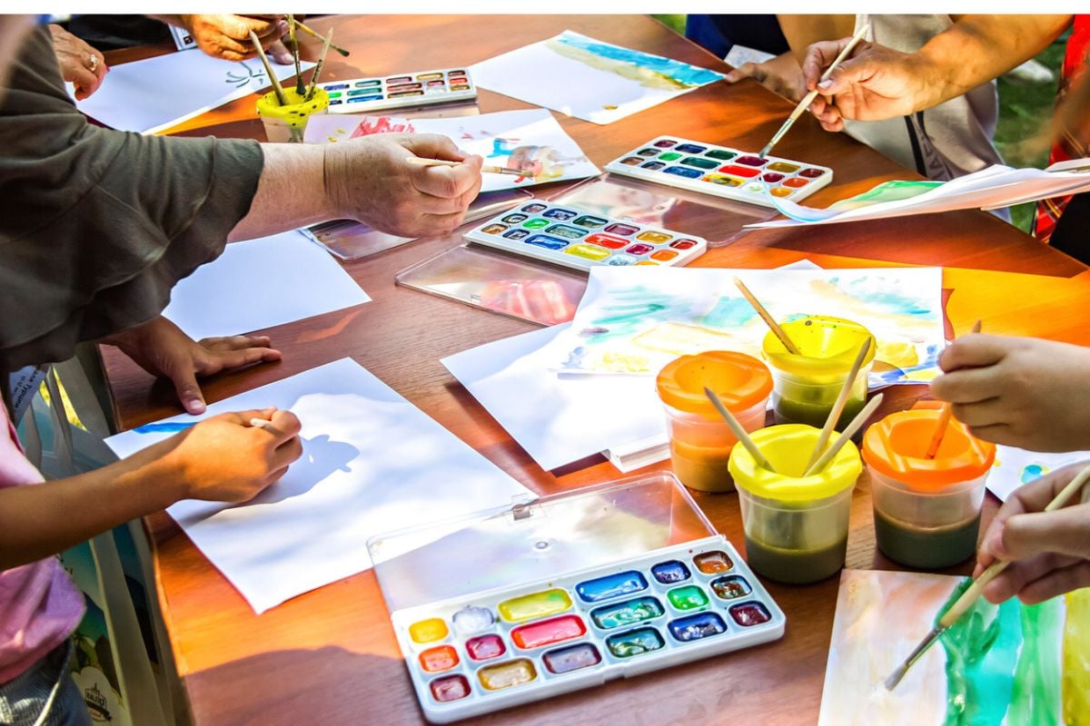 Several of people draw on paper using watercolor paints sitting at the same table. Drawing Masterclass. stock photo